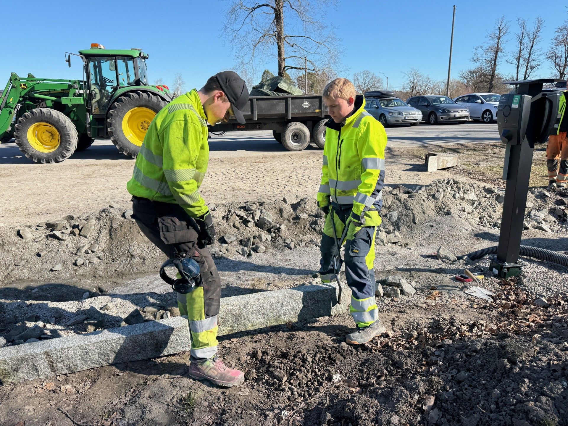 To elever løfter granittkantstein på plass i en grøft.