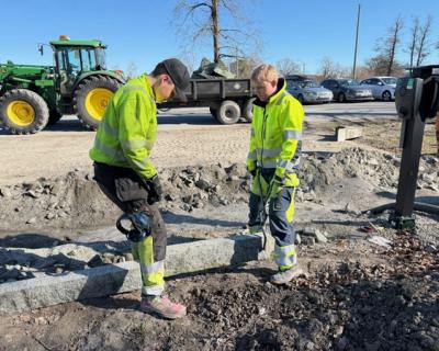 To elever løfter granittkantstein på plass i en grøft.