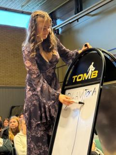 En ung kvinne står på en scene og skriver på en tavle.