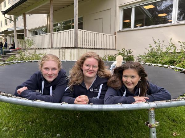 tre elevjenter ligger på en trampoline ute på en plen.
