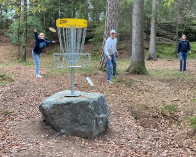 Tre ungdommer som forsøker å kaste disk i en golfkurv.