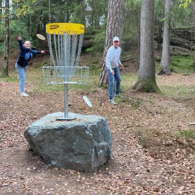 Tre elever forsøker å kaste frisbee i en golfkurv.