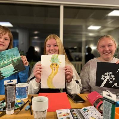 Tre jenter viser fram kunstverkene sine. 