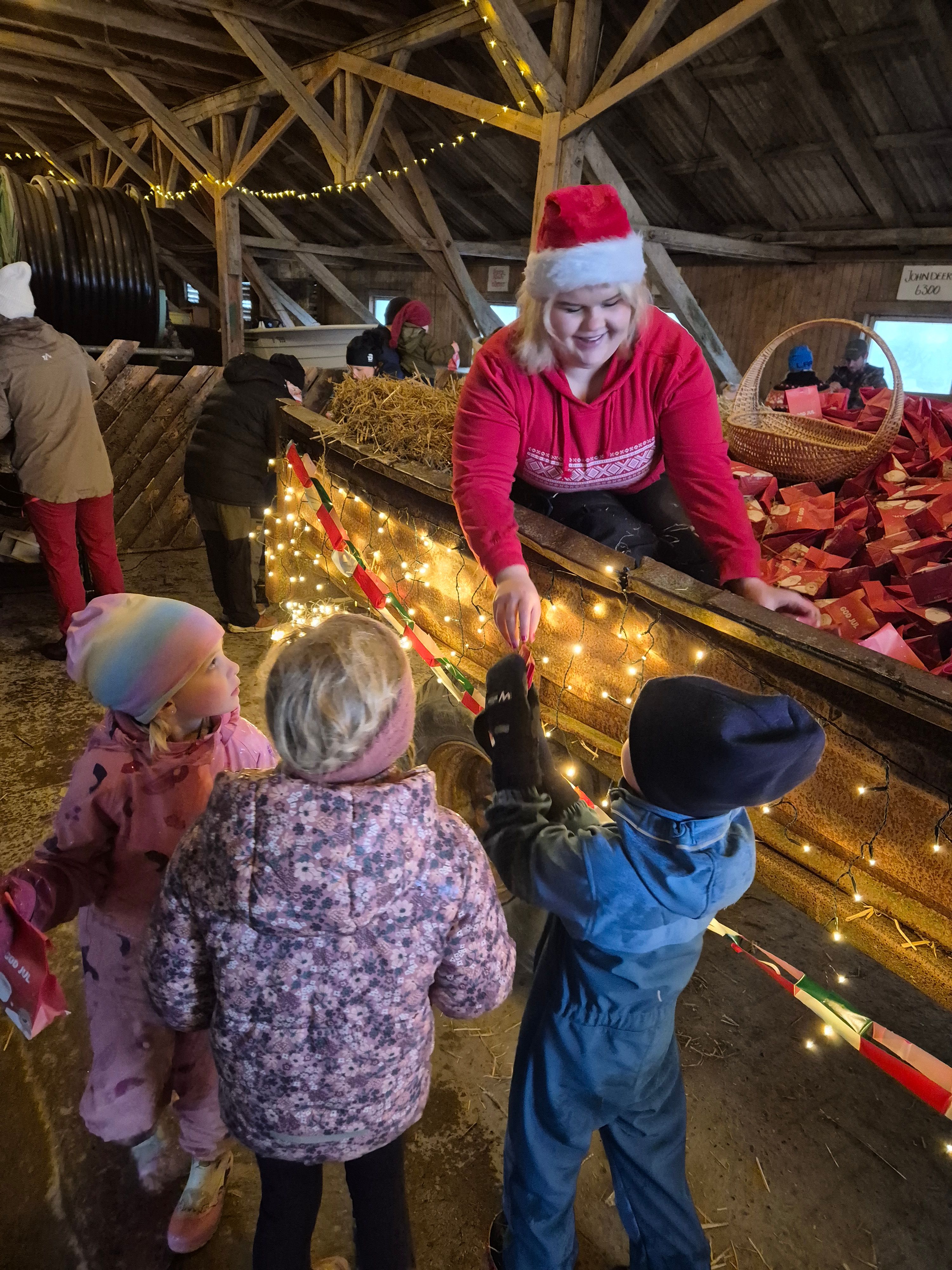 Jente utkledd som nisse sitter i en tilhenger og deler ut godteposer
