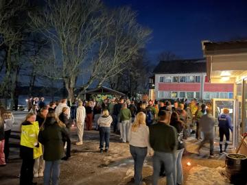 Masse ungdommer står på en åpen plass foran noen bygninger i kveldsmørke.