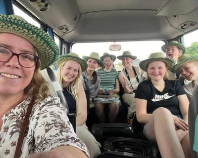 Bilde tatt inne i bussen, smilende folk med stråhatter.