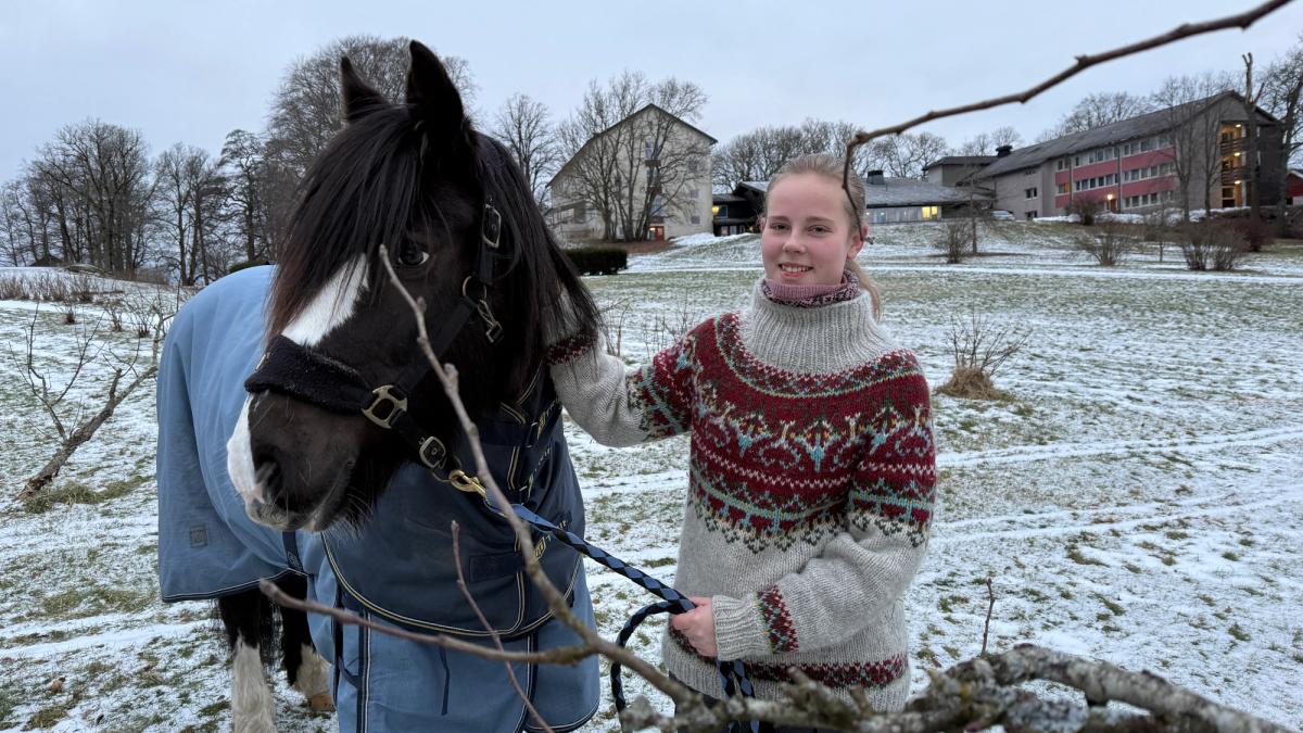 Jente står sammen med hest i en park. Delvis snø på gresset.