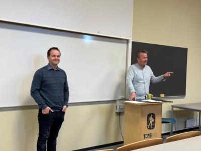 Lærer og rektor ved en lesepult ui et auditorium.