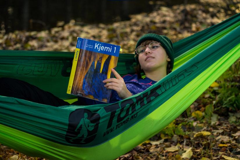 En ung jente ligger i hengekøye og leser i en kjemibok.