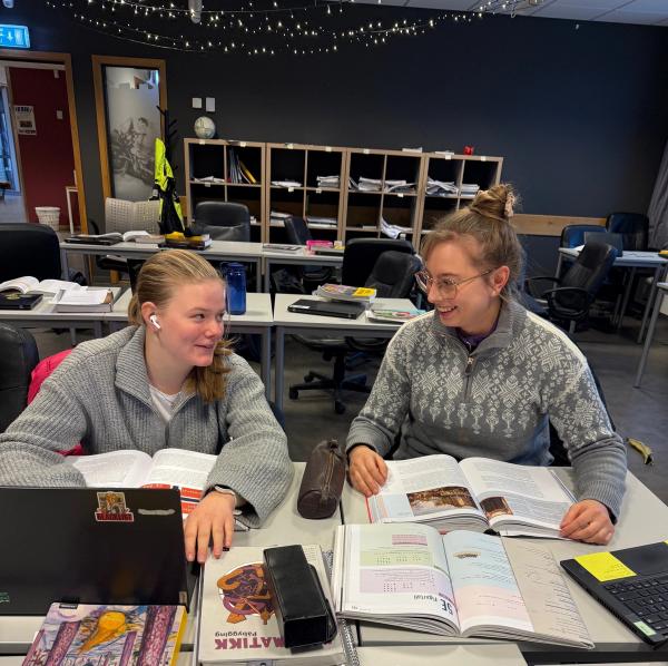 To elever sitter ved skolepulten i klasserommet og snakker sammen.