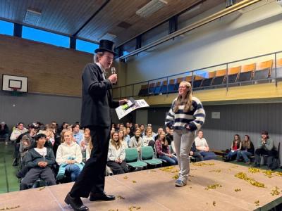 Ung mann i dress og flosshatt og kvinne snakker på en scene.