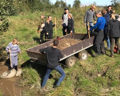 Elever skuffer sand  i bekken fra en tilhenger.
