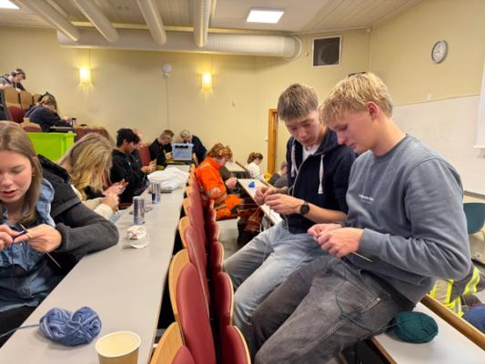 Elever som sitter i et auditorium og strikker.