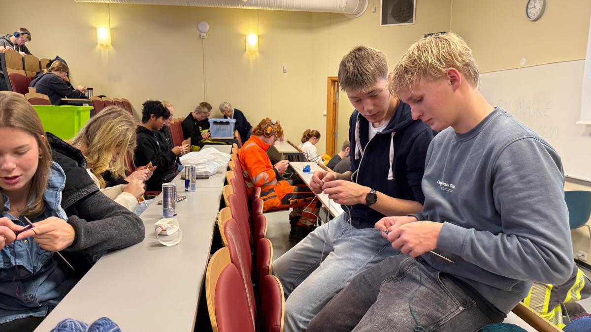 Elever som sitter i et auditorium og strikker.