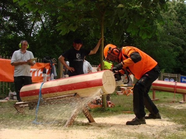 Mann med motorsag i motorsagutstyr skjærer en tømmerstokk.