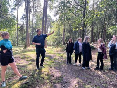 Læreren står ute i skogen og peker. 