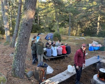 Elever rundt matbordet i skogen. Måltid forberedes på bålet.