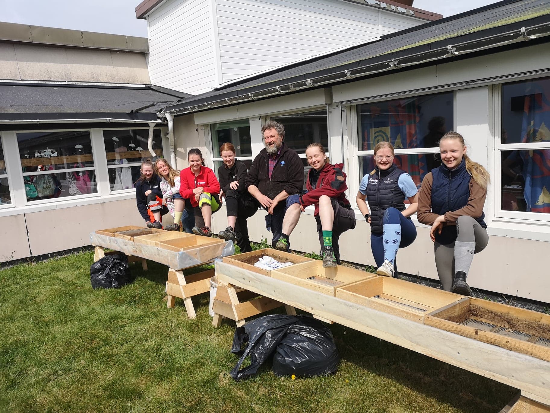 Jørgen og elevene med en fot hver oppå vekstkassene til skolehagen. 