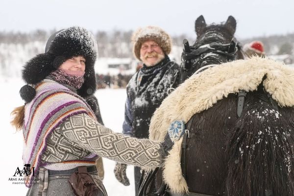 2 mennesker står godt påkledd ute en kald vinterdag sammen med en hest.