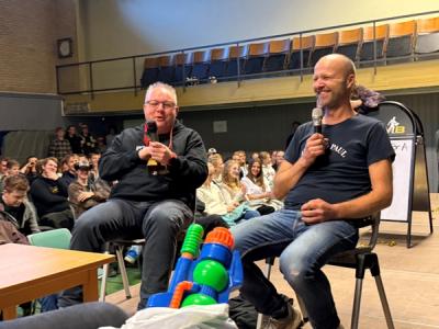 To lærere sitter på en scene og snakker i mikrofon.