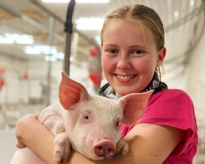 Jente som holder liten gris i armene.