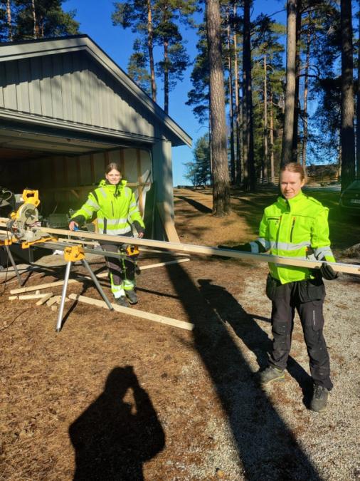 To jenter fra byggfag holder planker ved saga. 