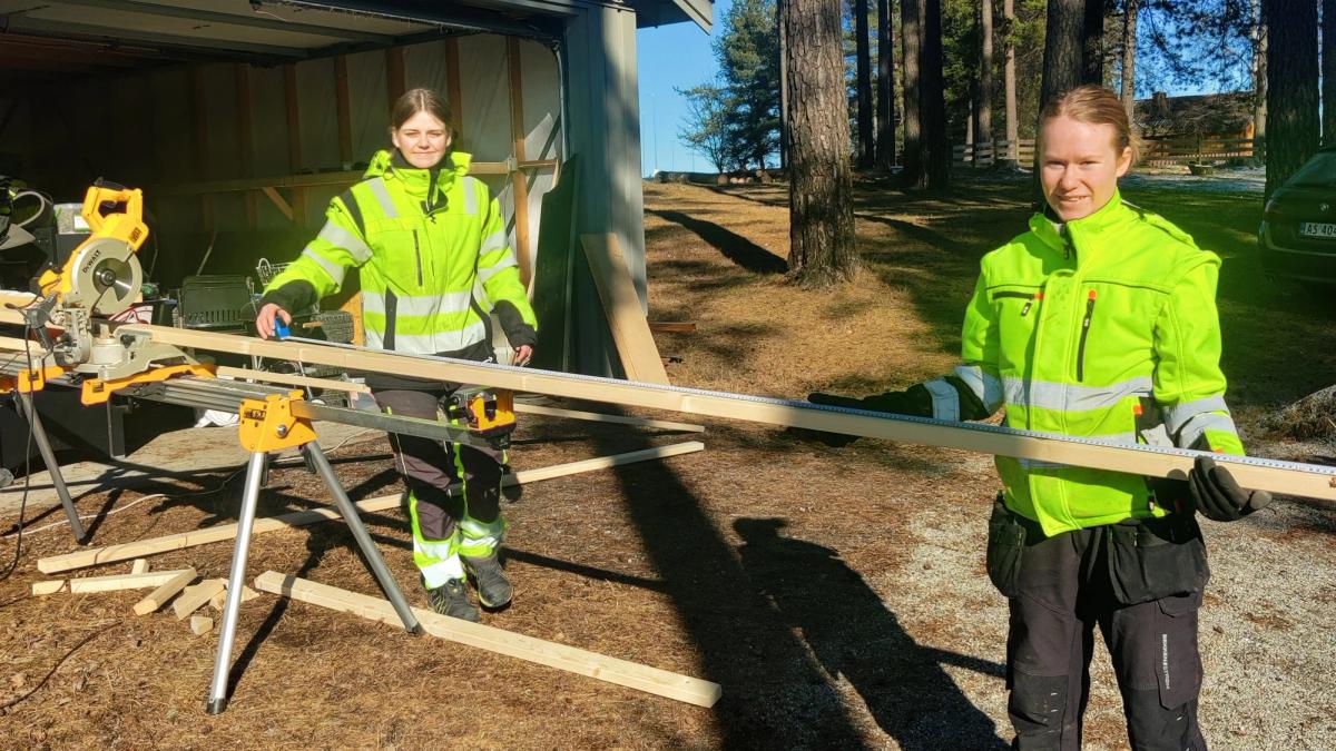 To jenter fra byggfag holder planker ved saga.