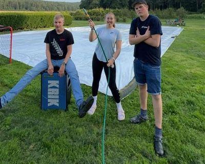 Tre elever i parken. I bakgrunnen en klargjort minifotball-bane med presenning som matte.