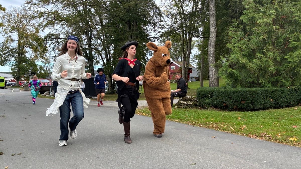 To elever løper på en vei sammen med en hundemaskot med brun pels, i voksen størrelse