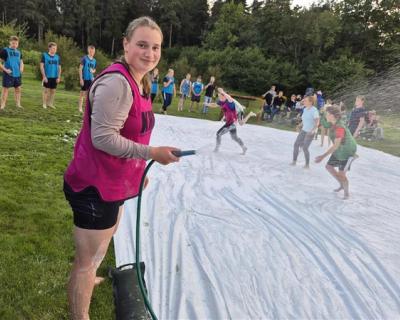 Elev spyler med slange. Såpefotball pågår på en presenning i bakgrunnen