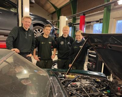 Fire elever smiler ved bil med åpent panser.