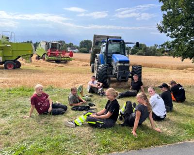 Elever som sitter ved kornåkeren - ved traktor og treskere.