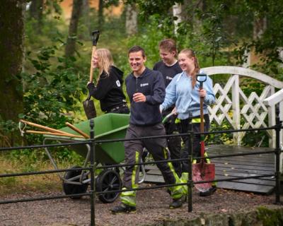 Fire elever med trillebår går over bru på Tomb