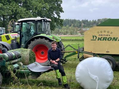 Gårdsarbeider sitter på en maskin i grasinnhøstingen. 