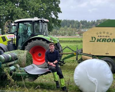 Gårdsarbeider sitter på en maskin i grasinnhøstingen.