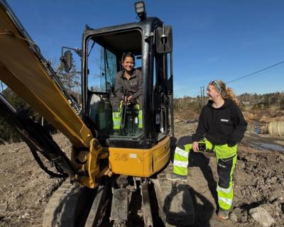 En elevjente sitter i en gravemaskin og en elevjente står utenfor maskinen.