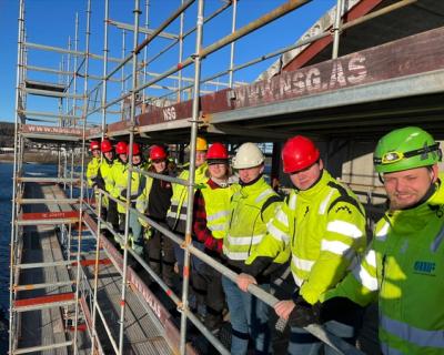 Mange byggfag-elever oppe i et stillas på et nybygg.