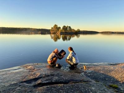 2 jenter sitter på et berg ved vannet.