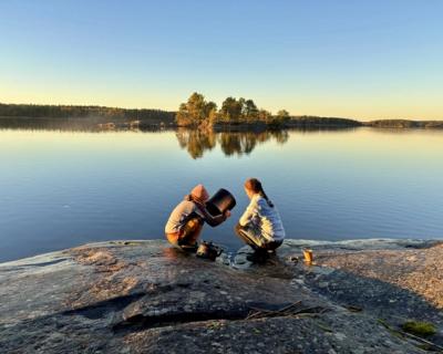 2 jenter sitter på et berg ved vannet.