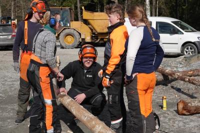 Elever i skogbruksklær jobber med en tømmerstokk.