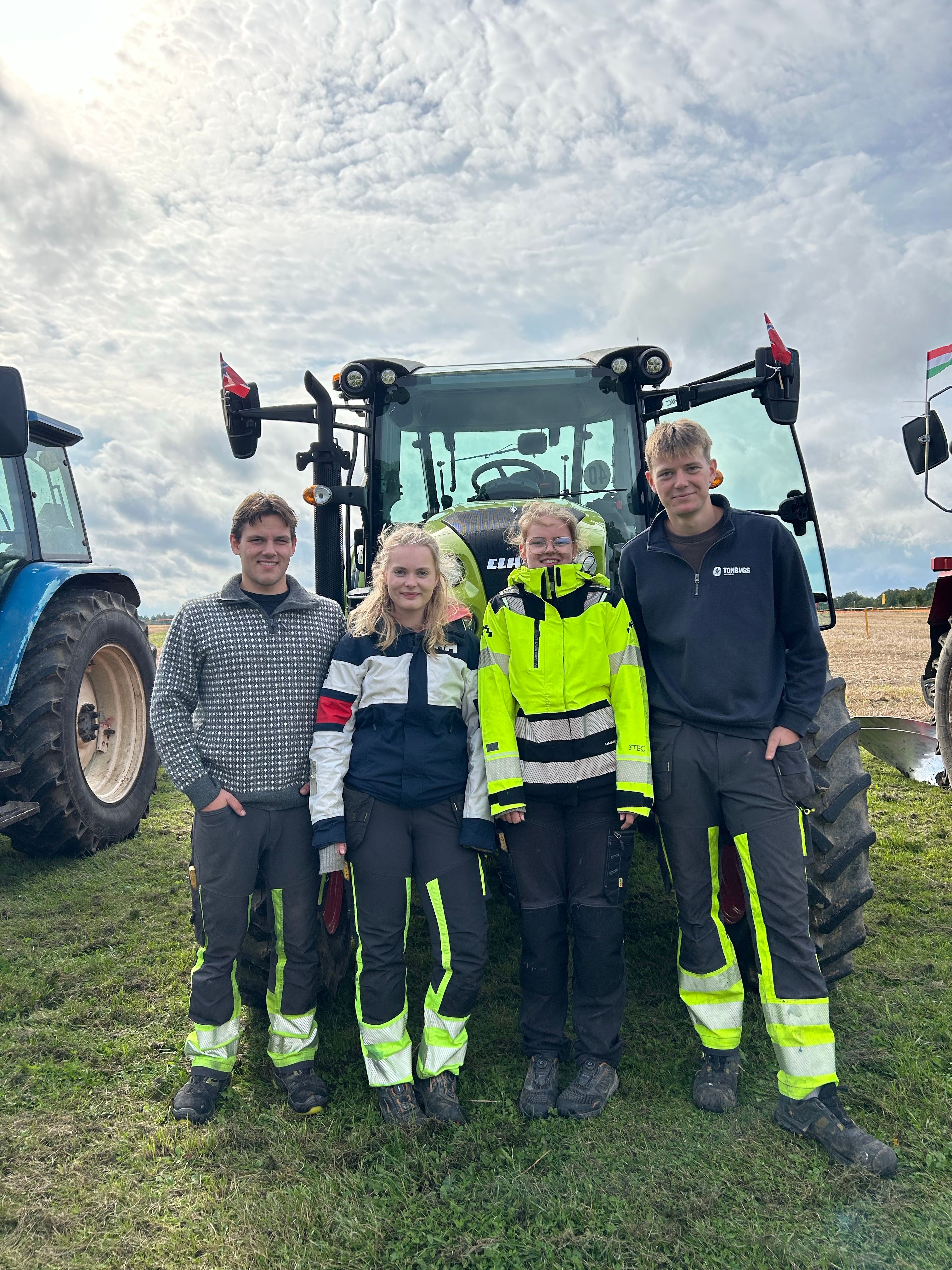 Fire elever står foran en traktor på et jorde.