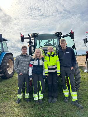 Fire elever står foran en traktor på et jorde.