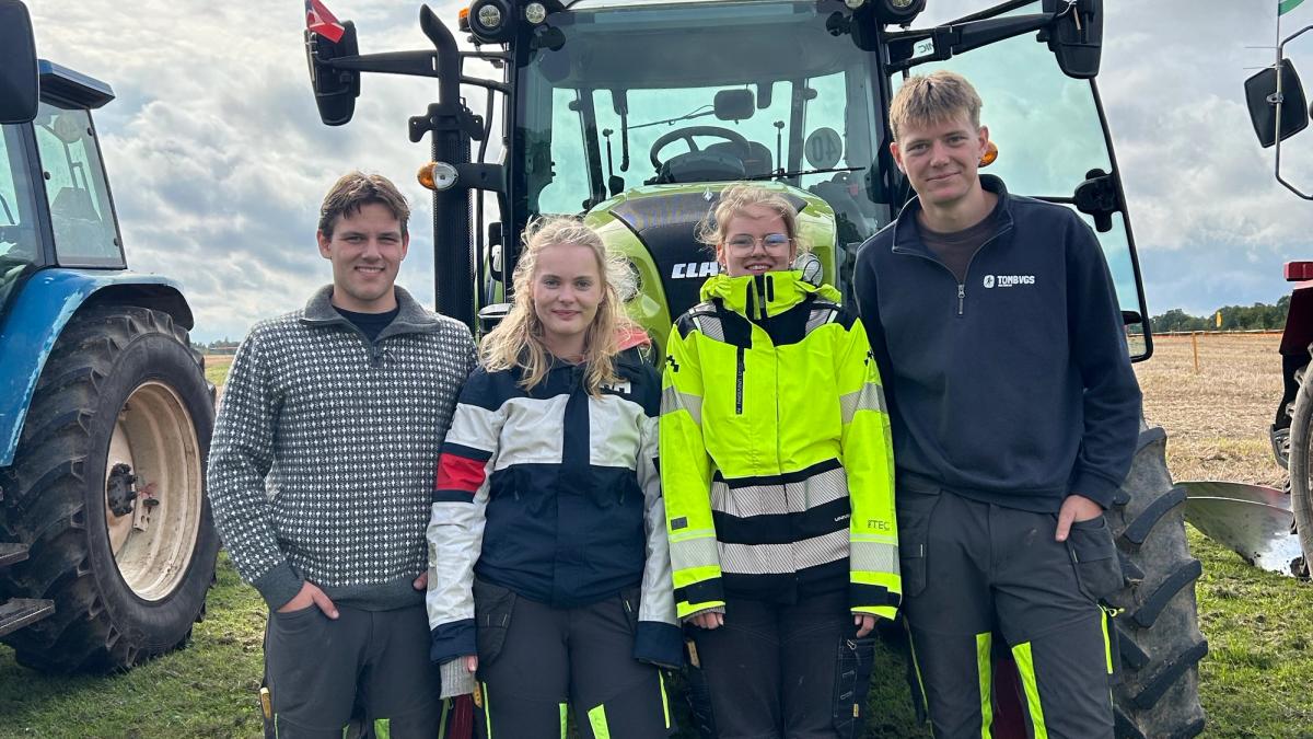Fire elever står foran en traktor på et jorde.