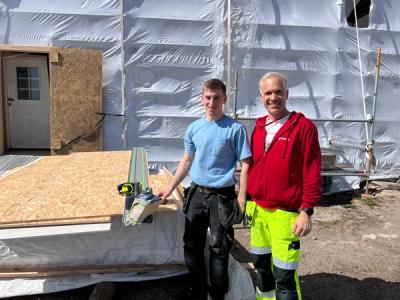 Byggfagelev og lærer foran et bygganlegg.