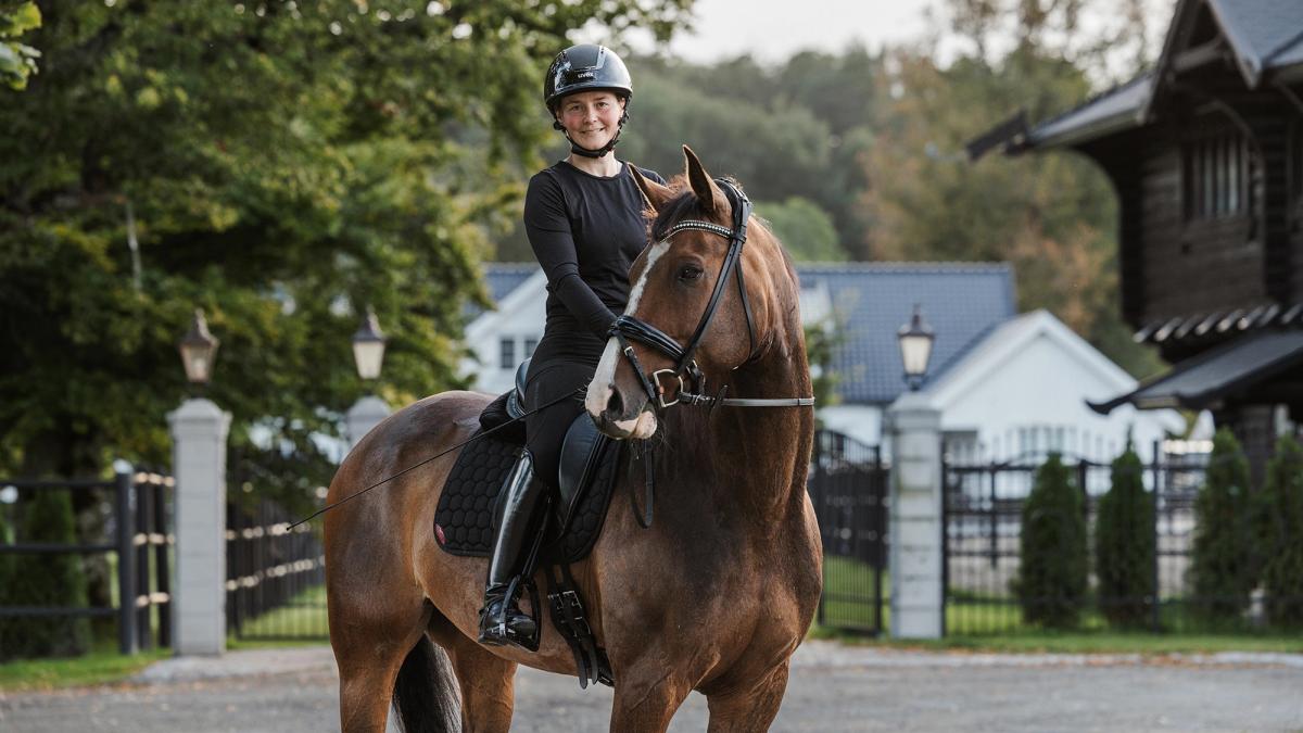 Henriette sitter på en hest, smiler mot kamera