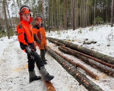 Elev og instruktør ved siden av tømmerstokker i skogen.