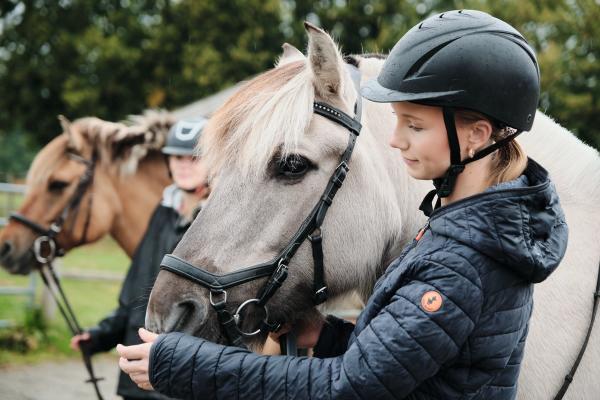 Jente som står og koser med mulen til hesten sin. 