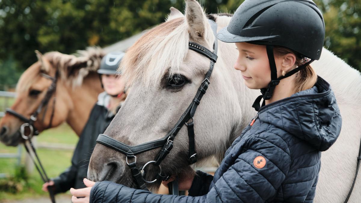 Jente som står og koser med mulen til hesten sin.