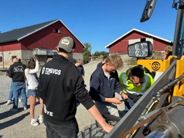 Flere elever står ute på en plass og studerer en hjullaster.