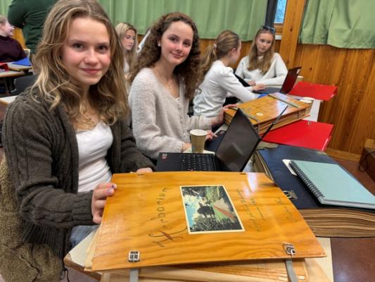 To jente-elever sitter i klasserommet og kikker på et gammelt herbarium.